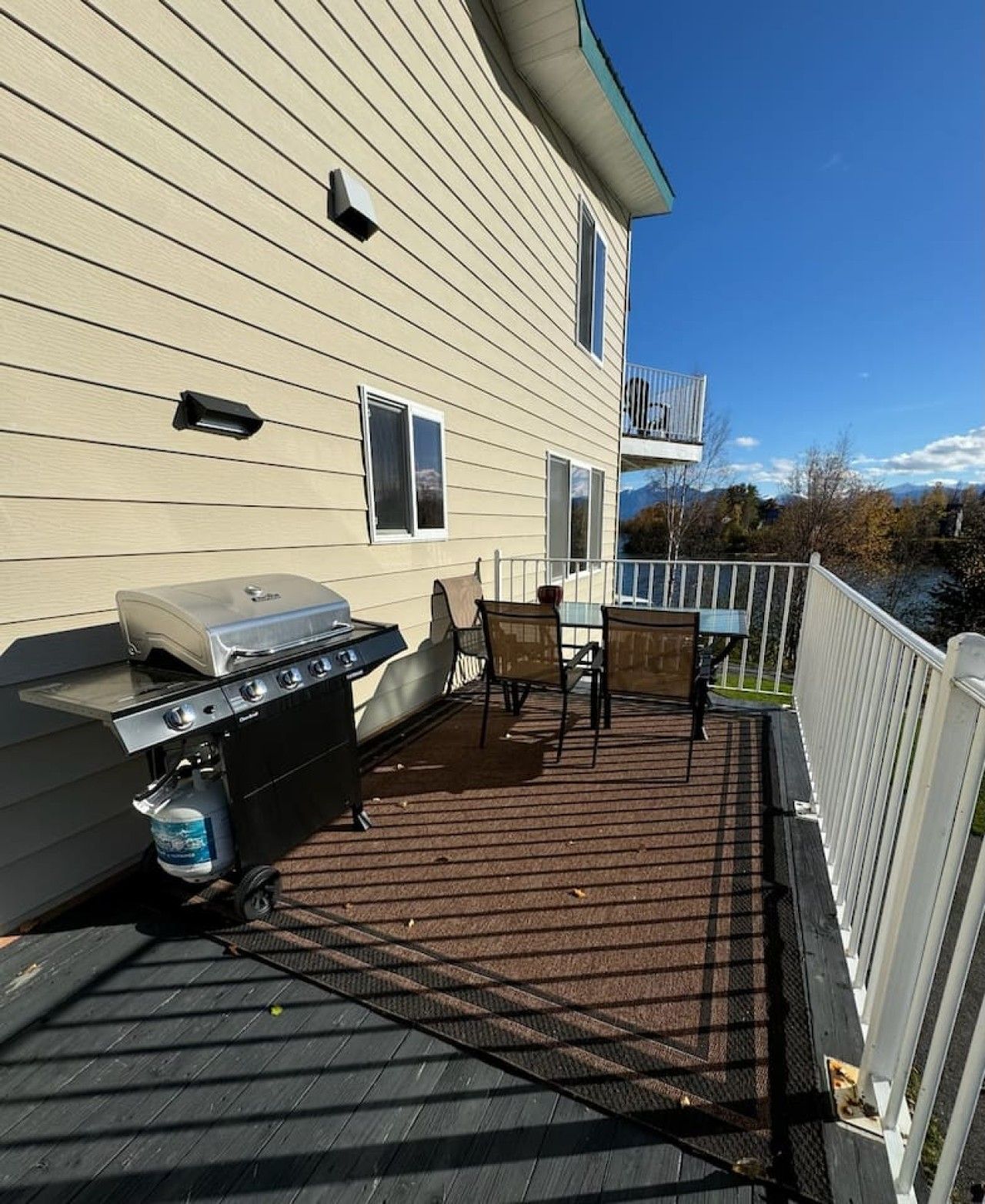 A deck with a grill, chairs, and a table.