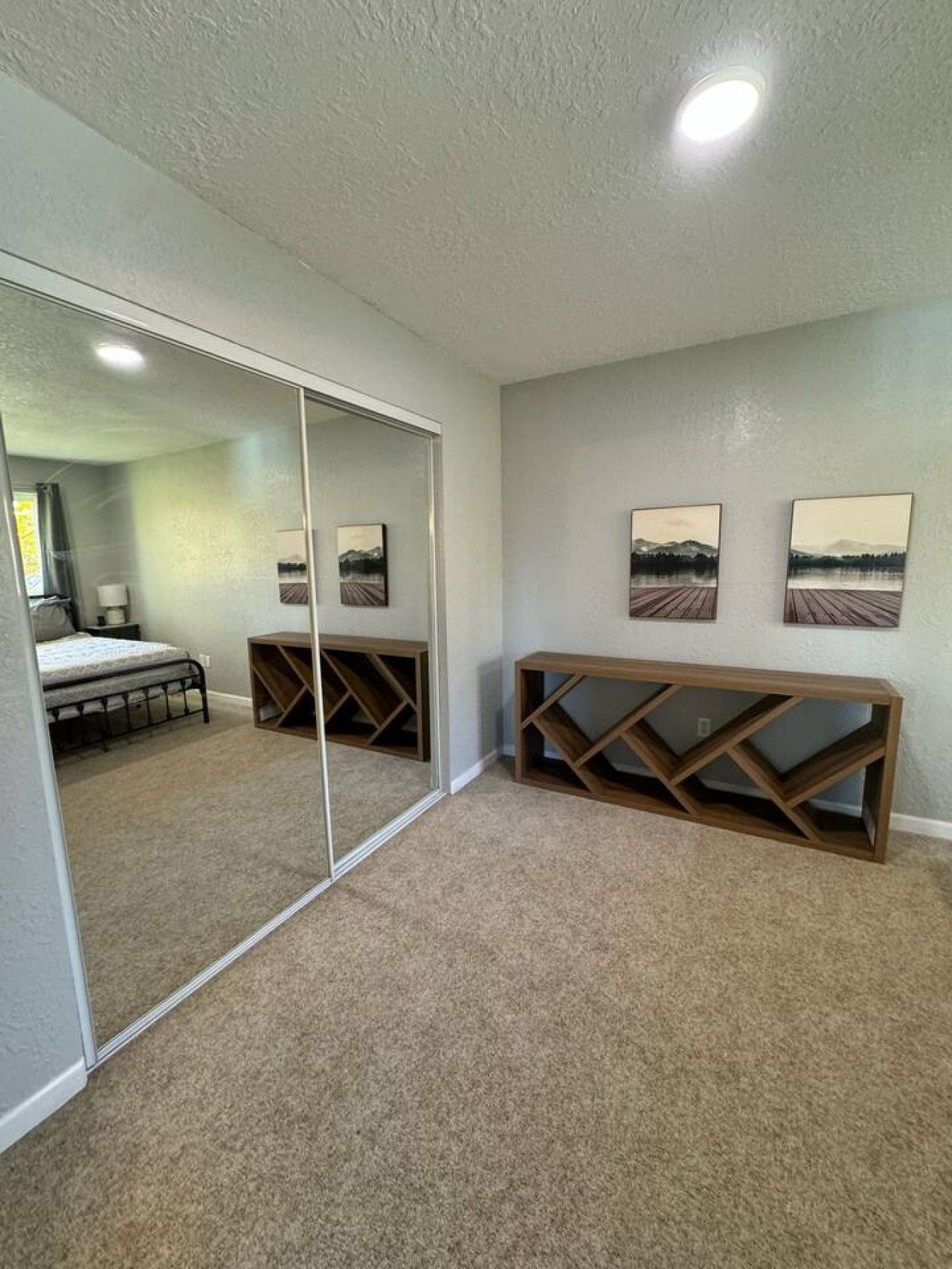 A bedroom with a large mirror, a bed, a wooden console table, and two landscape paintings on the wall.