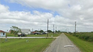 A rural road with houses on one side and a grassy area with a small building on the other. - Cozy campground in charming Alamo Beach, Texas (Alamo Beach)