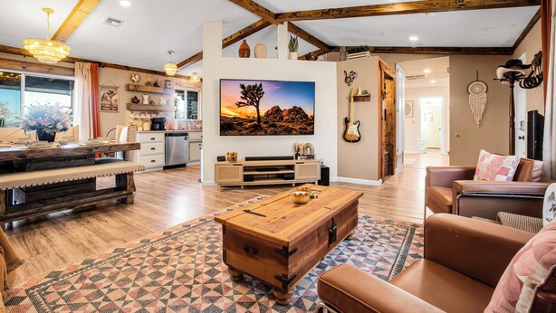A spacious living room with a wooden coffee table, a sofa, and a TV mounted on the wall. - JT Ranch: Observatory Sky Deck & Heated Cowboy Pool (Joshua Tree)