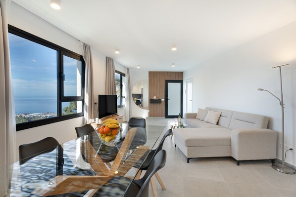 Un salon moderne avec une table à manger en verre, un canapé et une vue sur la mer.