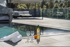 Un espace aménagé au bord de la piscine avec une bouteille d’alcool, deux verres et des serviettes enroulées.