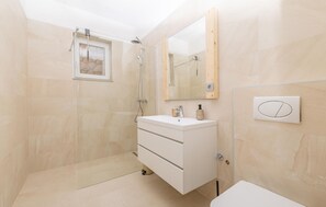 Un baño moderno con cabina de ducha, tocador con espejo y inodoro.