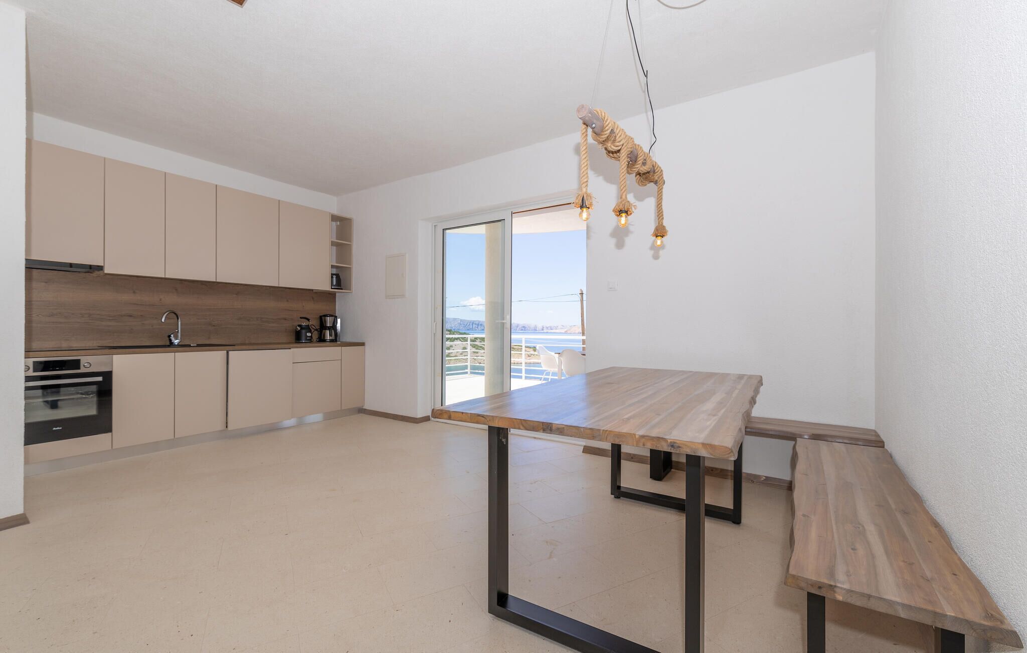 Une cuisine moderne dotée d’un plan de travail en bois, d’un four encastré et offrant une vue sur la mer grâce à une porte-fenêtre coulissante.