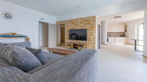 Een moderne woonkamer met een grijze bank, een flatscreen televisie bevestigd aan een stenen muur en een keuken op de achtergrond.