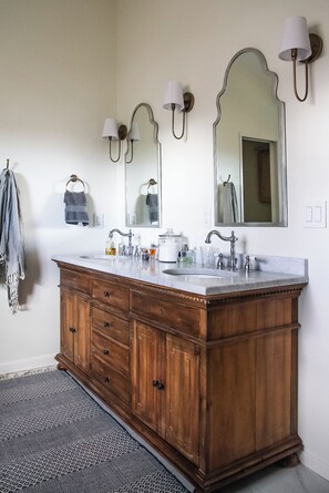 Une salle de bain avec un meuble-lavabo en bois, deux vasques, un grand miroir et des appliques murales.