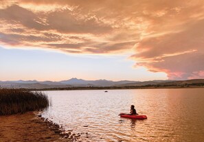 Un kayakiste sur un lac paisible, avec des montagnes en arrière-plan et un ciel au coucher du soleil.