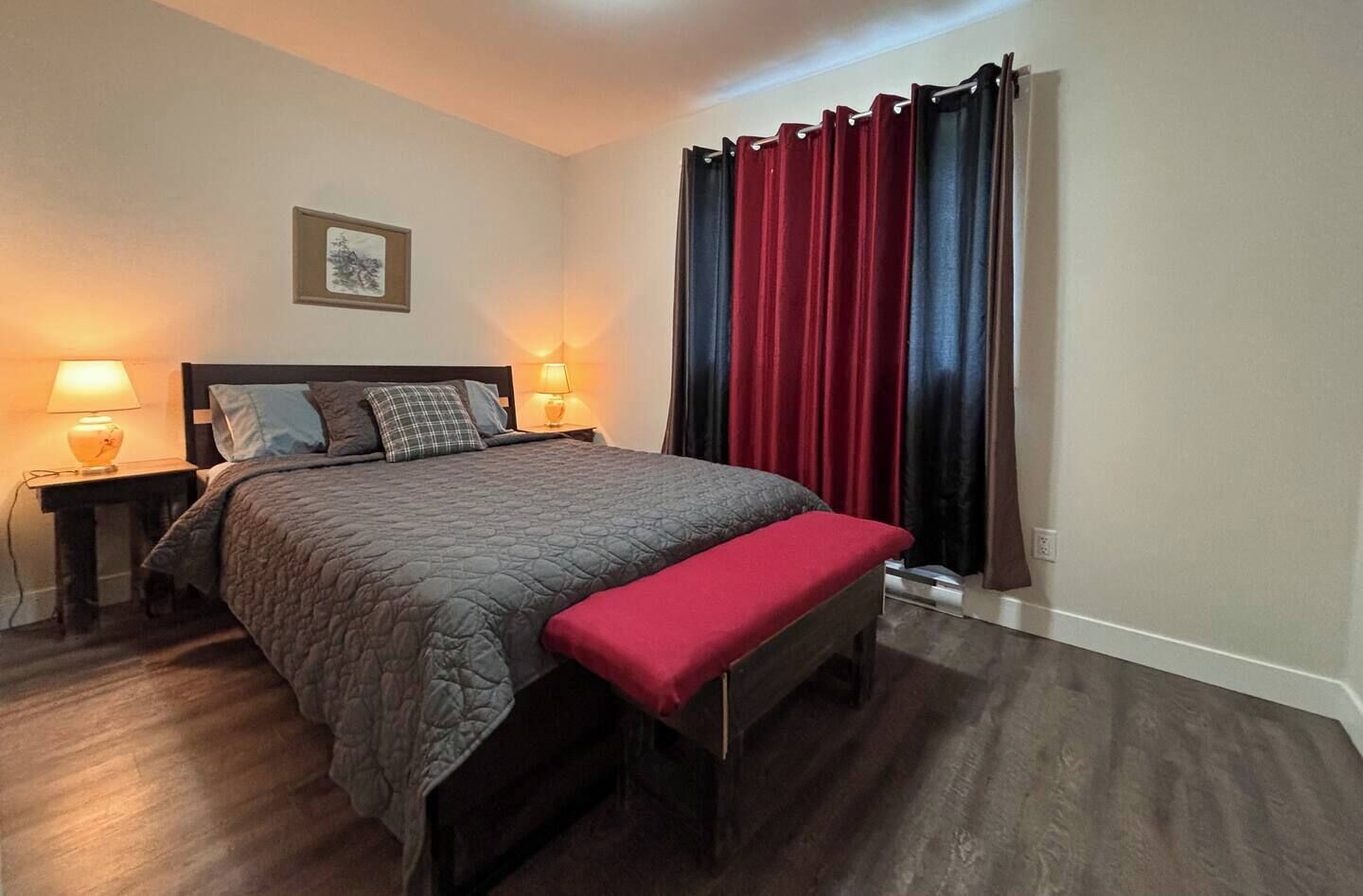 A neatly arranged bedroom with a bed, bedside lamps, a bench, and a window with curtains.