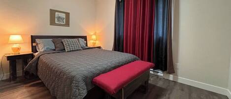 A neatly arranged bedroom with a bed, bedside lamps, a bench, and a window with curtains.