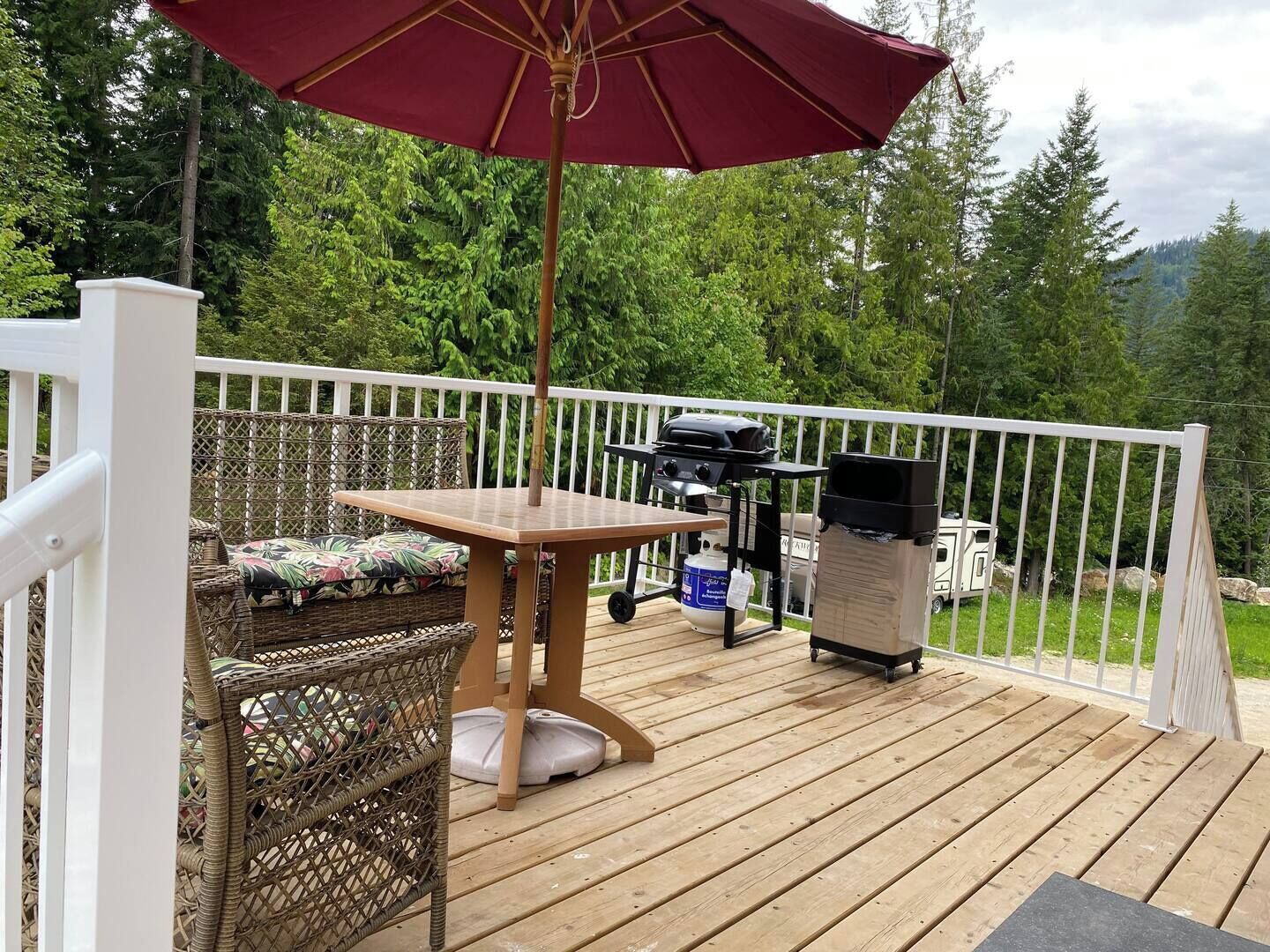 A wooden deck with a table and chairs, a grill, and a covered area with an umbrella.