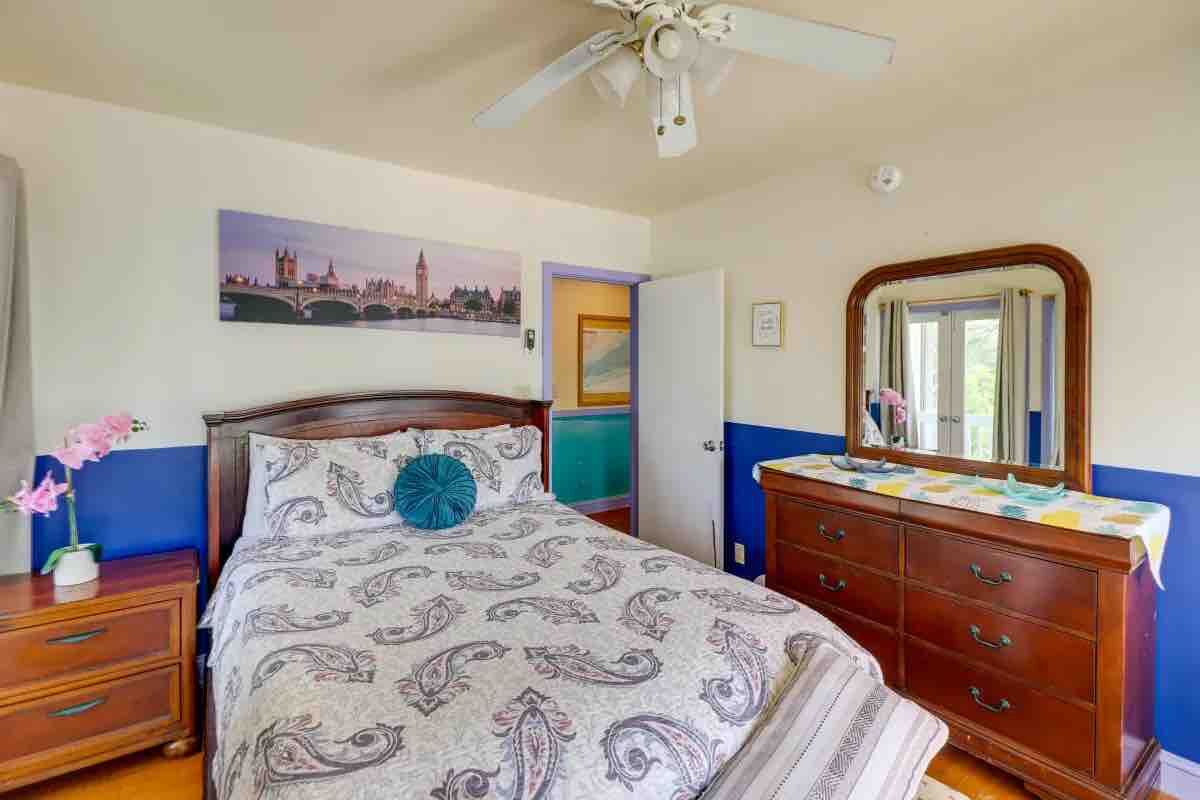Ein Schlafzimmer mit einem Bett, einem Schminktisch, einem Spiegel und einem Deckenventilator.