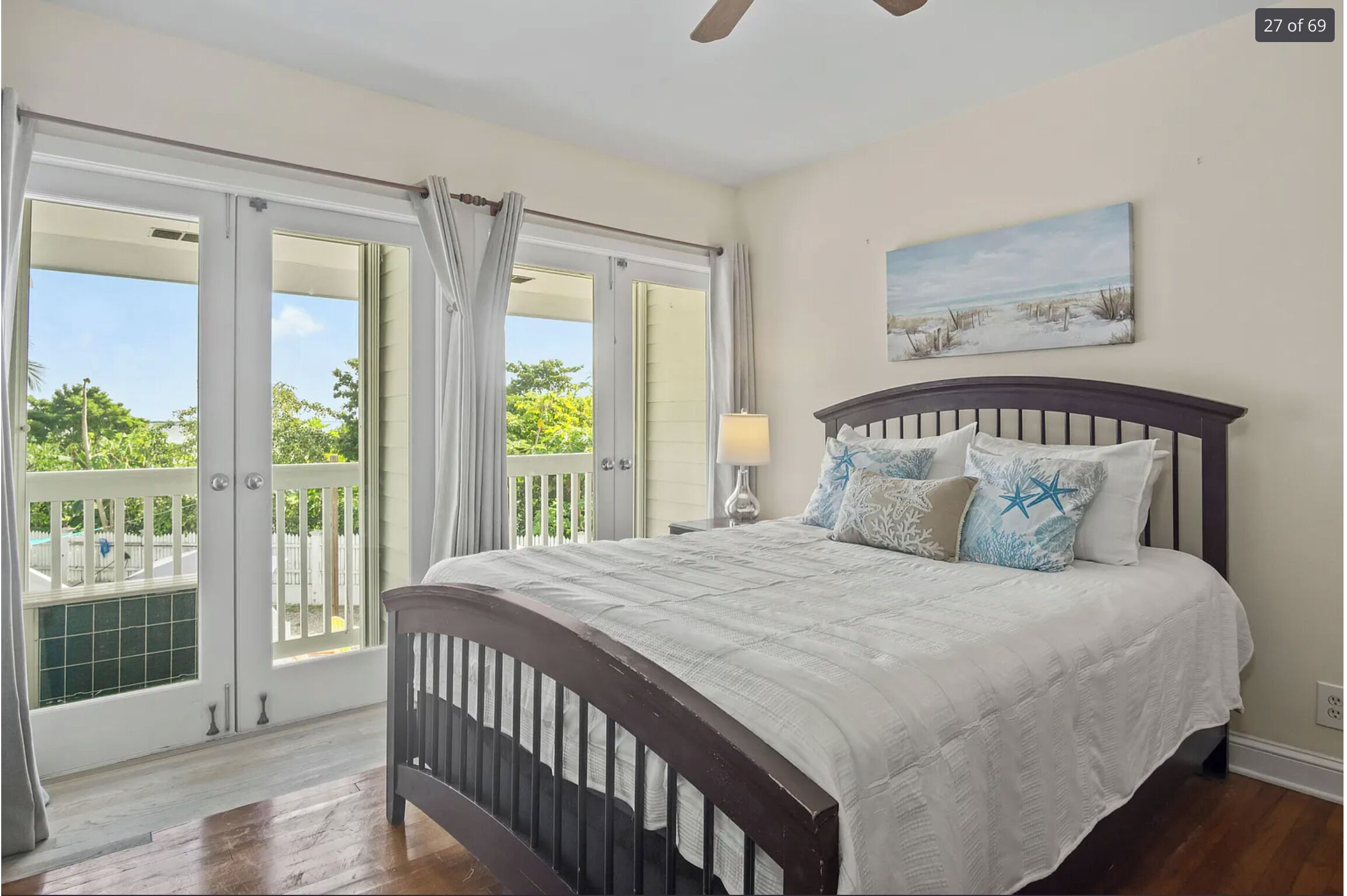 A bedroom with a bed, a nightstand, a painting, and a view through a sliding door.