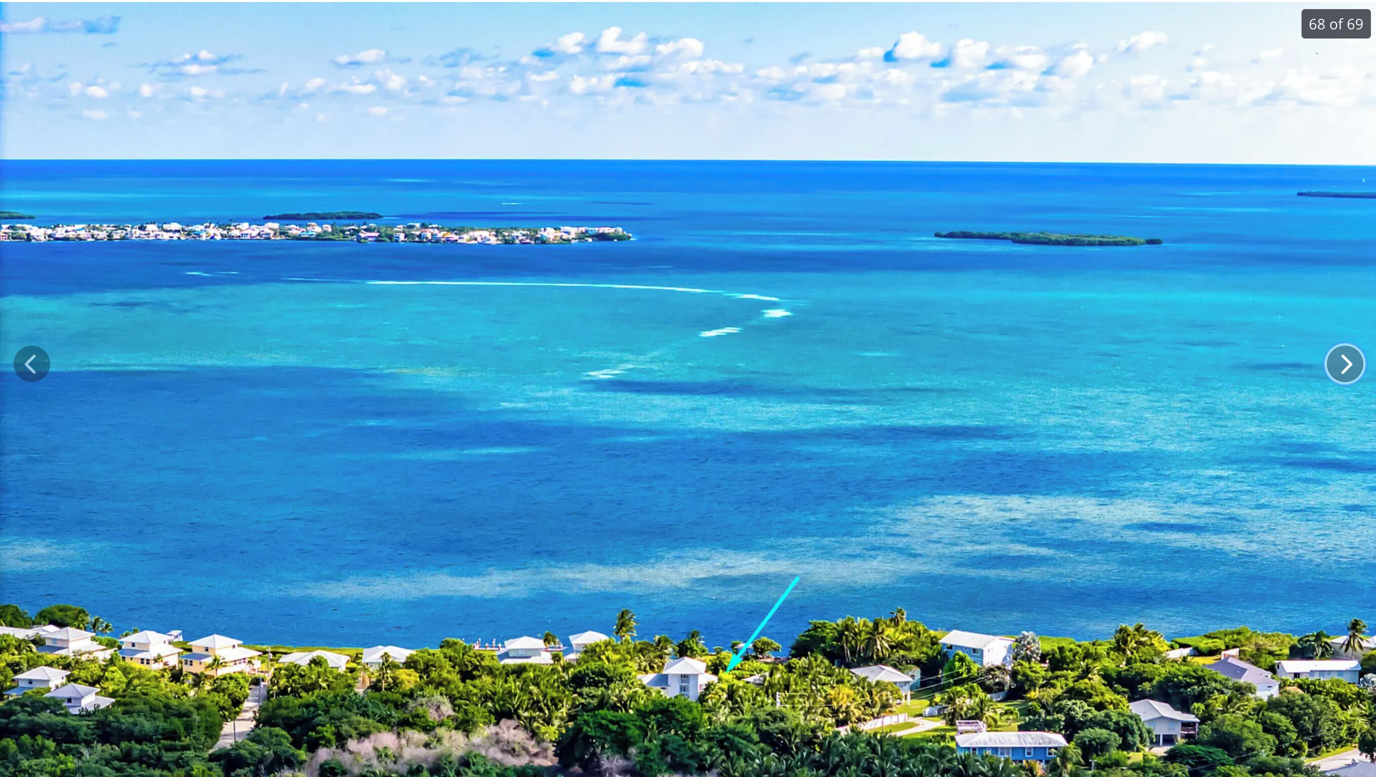 A coastal view with a clear blue sea, a small island with buildings, and a residential area with houses and greenery.