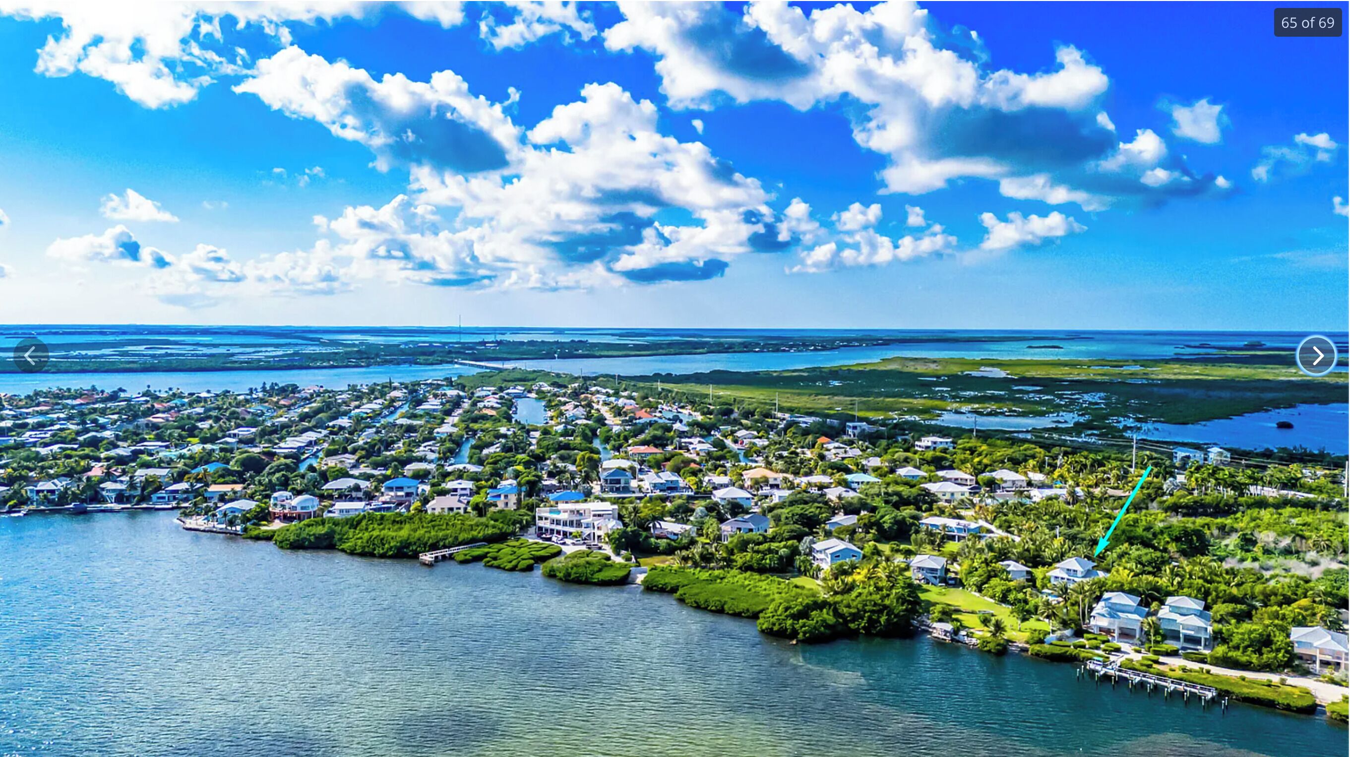 An aerial view of a coastal residential area with houses, a marina, and a clear blue sky.