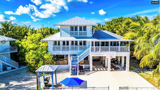Una casa fronte spiaggia su due piani con un balcone, un'area salotto esterna coperta e un piccolo molo per barche.