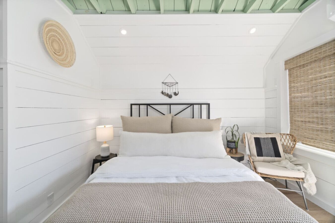 Un dormitorio con cama, mesita de noche, lámpara, adorno de pared y ventana con persianas.