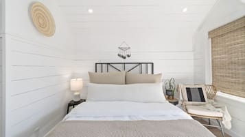 Un dormitorio con cama, mesita de noche, lámpara, adorno de pared y ventana con persianas.