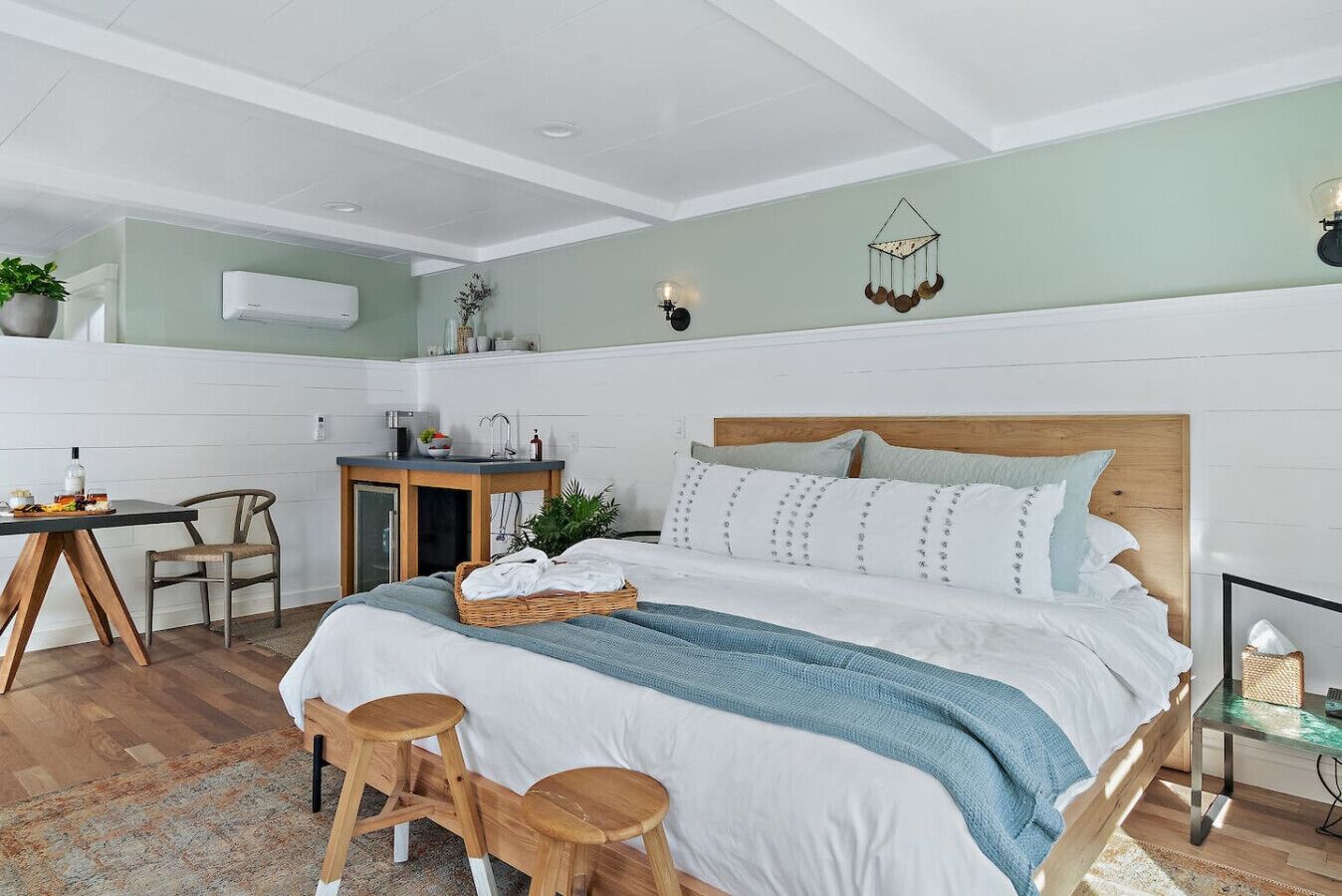 Un dormitorio con una cama grande, una mesita de noche, una silla, un escritorio pequeño y un aire acondicionado de pared.