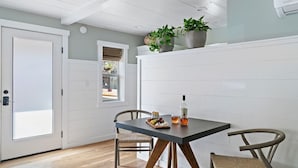 A dining area with a table, chairs, a potted plant, and a window. - The Deckhouse | Avila Beach · Steps to Sand (Avila Beach)