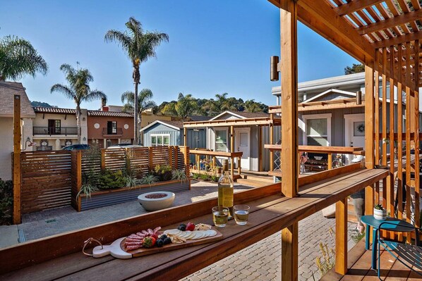 A wooden deck with a food and drink setup, surrounded by residential buildings and palm trees.