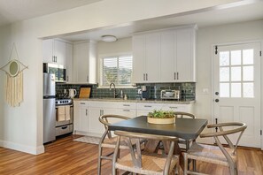 A kitchen with white cabinets, a stove, a sink, and a dining area with a table and chairs.