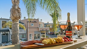 A balcony with a wooden cutting board, sliced fruits, a bottle of wine, and glasses.