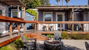 A wooden deck with outdoor seating, a fire pit, and a view of a residential building with a covered porch.