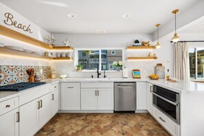 Een moderne keuken met witte kasten, een RVS vaatwasser en een groot raam.
