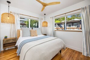 A bedroom with a large bed, wooden headboard, a ceiling fan, and a window with curtains. - La Casita — Designer 2BR Beach House Less Than a Block from the Sand | Gas Fireplace · Soaking Tub & Rainfall Shower · Gourmet Kitchen · In-Unit Laundry · Two Parking Spots · Sleeps 6 · Avila Beach · Managed by Solmaré Stays (Avila Beach)