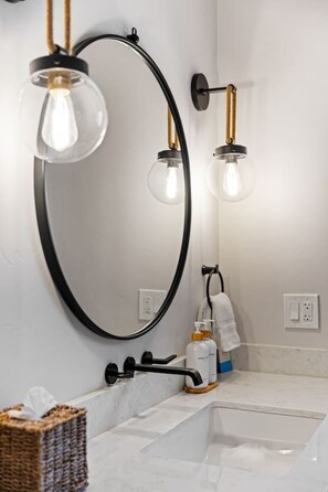 A bathroom with a large mirror, two pendant lights, a towel rack, and a sink. - La Casita — Designer 2BR Beach House Less Than a Block from the Sand | Gas Fireplace · Soaking Tub & Rainfall Shower · Gourmet Kitchen · In-Unit Laundry · Two Parking Spots · Sleeps 6 · Avila Beach · Managed by Solmaré Stays (Avila Beach)