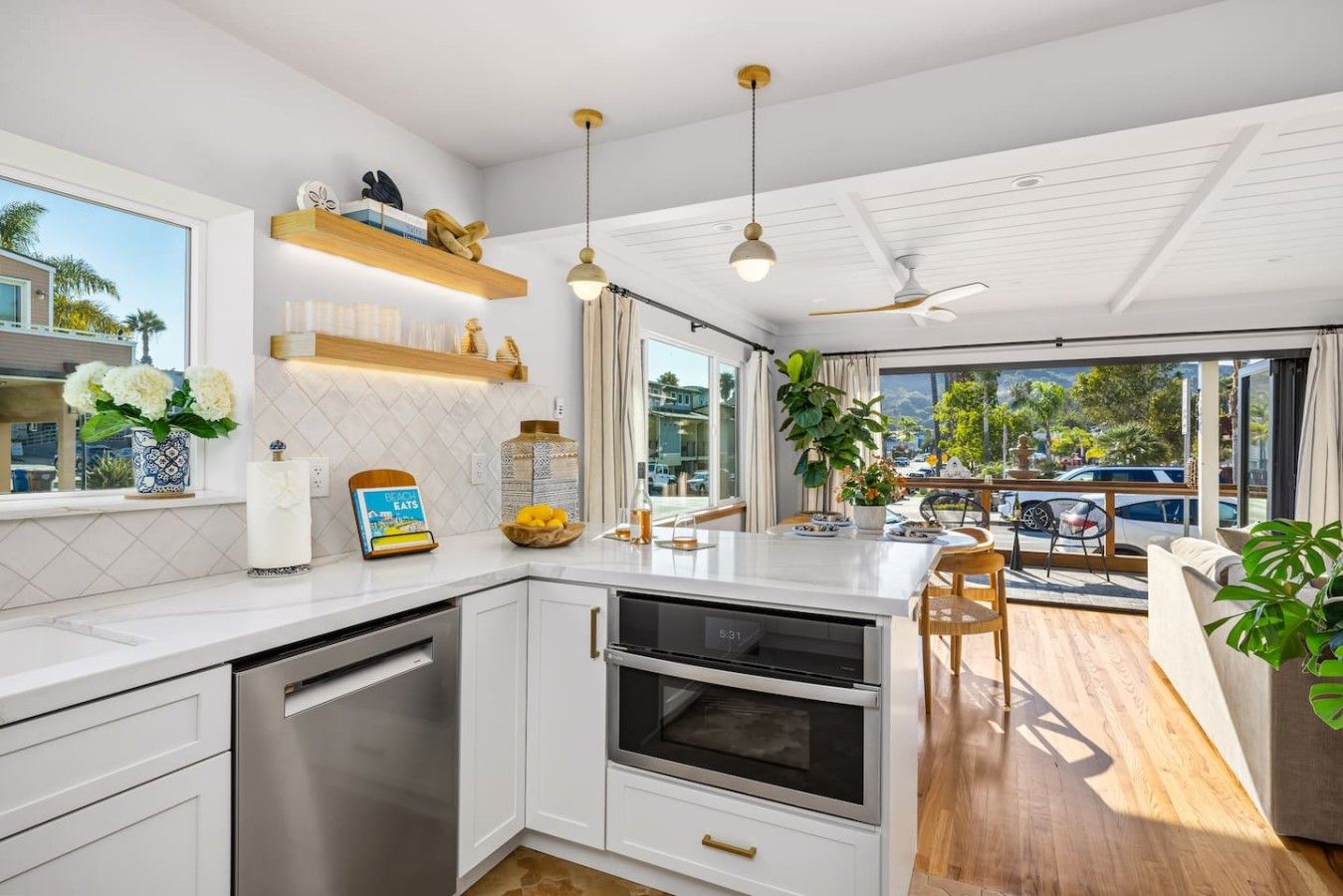 A modern kitchen with white cabinetry, a built-in oven, and a dining area with a wooden table and chairs.