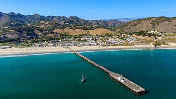 A coastal town with a long pier extending into the sea, surrounded by hills and a beach.