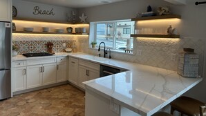 Una cocina moderna con armarios blancos, encimera de mármol y salpicadero con diseño de playa.