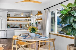 A modern kitchen with white cabinets, a wooden dining table, and a large window with a view. - La Casita — Designer 2BR Beach House Less Than a Block from the Sand | Gas Fireplace · Soaking Tub & Rainfall Shower · Gourmet Kitchen · In-Unit Laundry · Two Parking Spots · Sleeps 6 · Avila Beach · Managed by Solmaré Stays (Avila Beach)