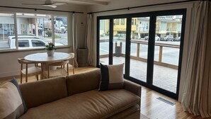 Una sala de estar con un sofá, una mesa redonda y vista a la calle a través de ventanas amplias.
