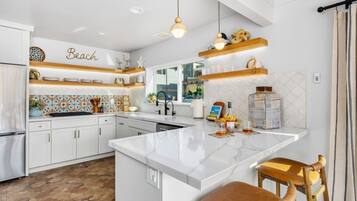 A modern kitchen with white cabinetry, a marble island, and decorative items on shelves.