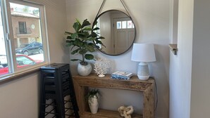 Habitación de esquina con una consola de madera, un espejo colgado, una planta en maceta, una lámpara y un pequeño estante con adornos.
