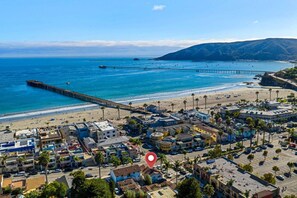 A coastal town with a pier extending into the sea, beachfront properties, and a clear sky. - La Casita — Designer 2BR Beach House Less Than a Block from the Sand | Gas Fireplace · Soaking Tub & Rainfall Shower · Gourmet Kitchen · In-Unit Laundry · Two Parking Spots · Sleeps 6 · Avila Beach · Managed by Solmaré Stays (Avila Beach)