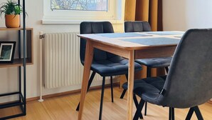 Ett modernt rum med ett träbord, svarta stolar, ett element, ett fönster med utsikt över träd och en krukväxt på en hylla.