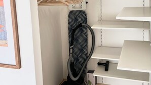 En garderob med vita hyllor, en dammsugare och en inramad tavla på väggen.