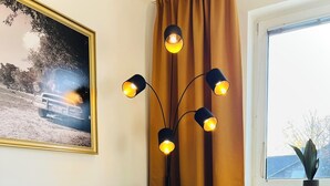 Ett modernt vardagsrum med en grå soffa, gula kuddar, ett litet träbord med en fjärrkontroll och ett glas mjölk, och en golvlampa med tre lampor.