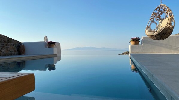 Una piscina infinita tranquila con vistas despejadas a montañas lejanas, una silla colgante y una pared de piedra.
