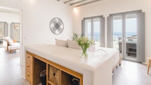 A modern bedroom with a large bed, a wooden cabinet, a vase with flowers, and a view of the sea through large windows. - Villa Camelia 1 - 1BR - Private Pool & Jacuzzi - Sea View - Psarou (Nammos) (Mykonos)