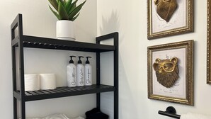 Ein Badezimmer mit einem schwarzen Regal, das Toilettenartikel, eine Topfpflanze und gerahmte Kunstwerke beherbergt.