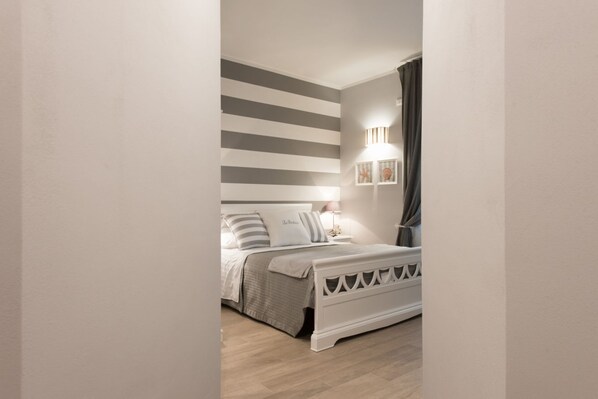 A bedroom with a bed, a nightstand, a wall-mounted lamp, and a curtain.