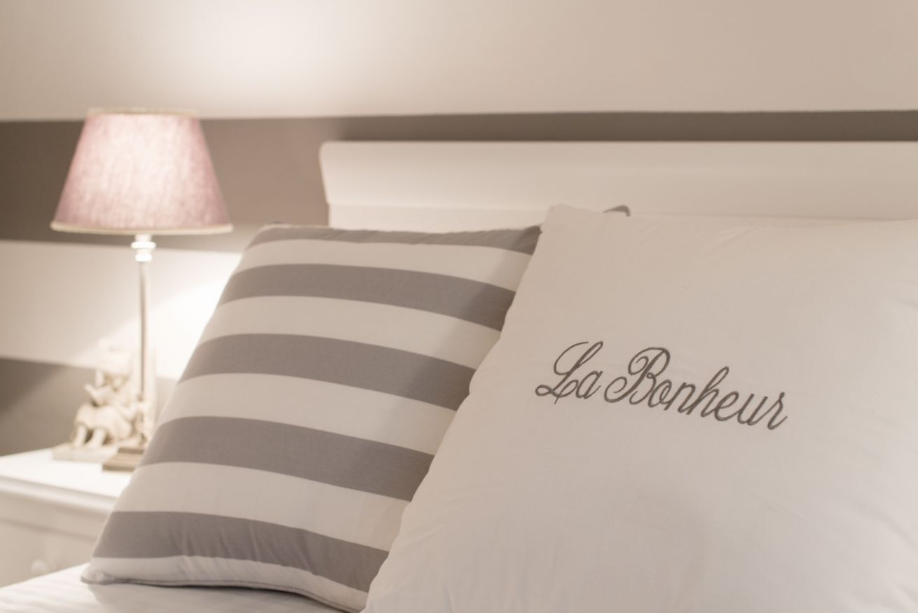 A bed with striped pillows and a pillow with "La Bonheur" embroidered on it.