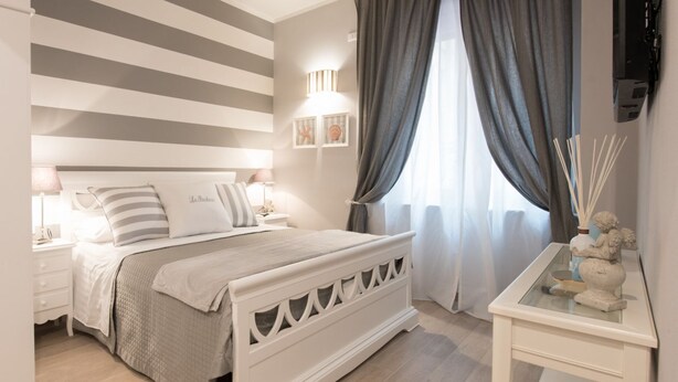 Un dormitorio con cama, mesitas de noche, un espejo y una ventana con cortinas.