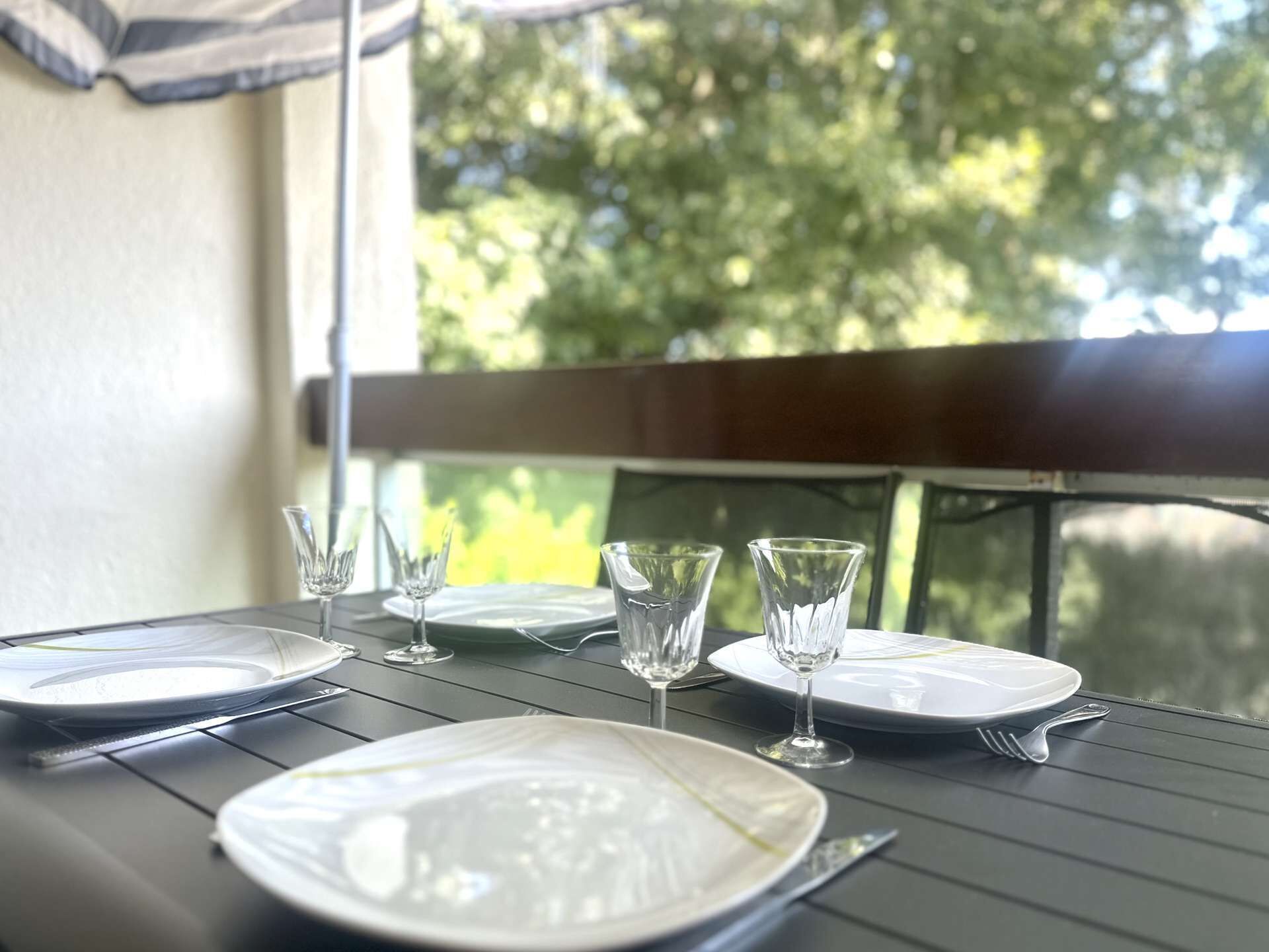 A dining table set with plates, glasses, and cutlery, positioned near a window with a view of trees.