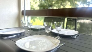 Une table à manger est dressée avec des assiettes, des verres et des couverts, et est placée près d’une fenêtre d’où l’on peut admirer les arbres.