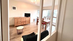 Une pièce comprenant un meuble en bois, un téléviseur, une table à manger avec des chaises et une fenêtre.